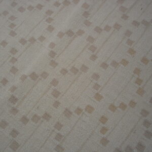 A light beige rug with a subtle, textured diagonal pattern of small, scattered taupe squares.
