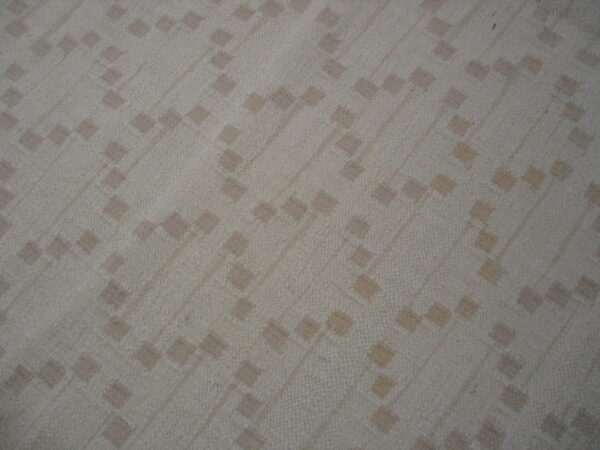 A light beige rug with a subtle, textured diagonal pattern of small, scattered taupe squares.