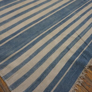 A flatweave rug with wide blue and cream diagonal stripes sits on rough hardwood planks.