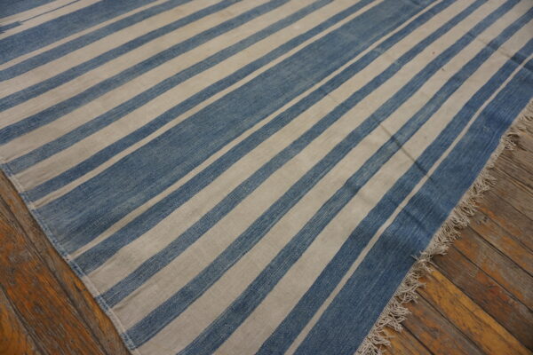 A flatweave rug with wide blue and cream diagonal stripes sits on rough hardwood planks.