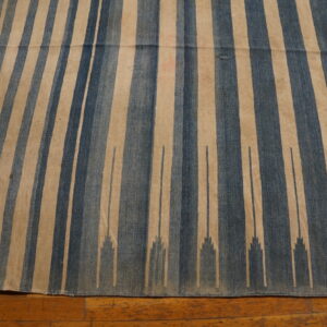Flat-weave rug with vertical blue and tan stripes featuring a stepped design on a hardwood floor.
