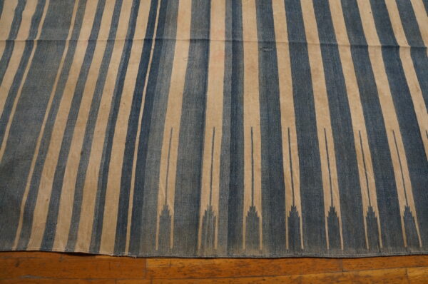 Flat-weave rug with vertical blue and tan stripes featuring a stepped design on a hardwood floor.