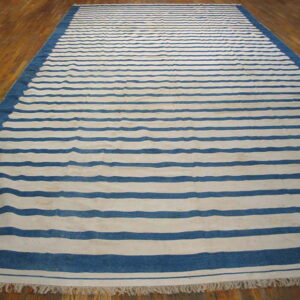 Blue and white striped rug with a solid border and fringe, displayed on polished wood flooring.