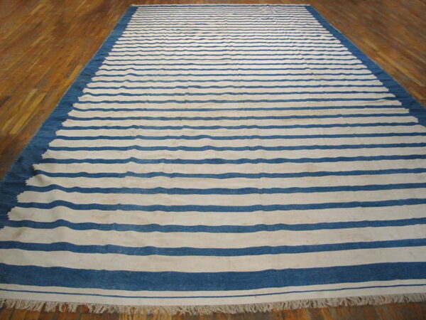 Blue and white striped rug with a solid border and fringe, displayed on polished wood flooring.