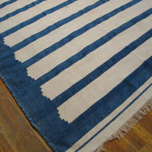 Blue and cream flatweave rug with wide stripes and a serrated border lying on wood floors.