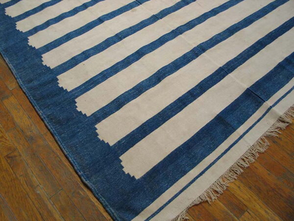 Blue and cream flatweave rug with wide stripes and a serrated border lying on wood floors.