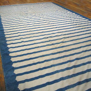 Blue and white horizontally striped flatwoven rug with a wide solid border on a wooden floor.