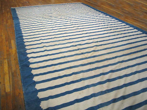 Blue and white horizontally striped flatwoven rug with a wide solid border on a wooden floor.