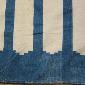 Blue and cream striped flatweave rug showing a stepped edge design resting on a wooden floor.