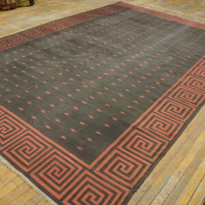 Large dark rug with a red-orange Greek key border and dashed pattern on light wood flooring.