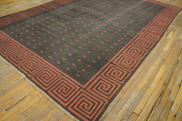 Dark flatwoven rug with rust key border and scattered geometric motifs on worn wood floors.