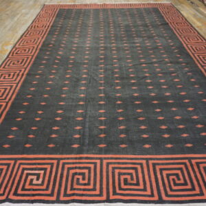 Large dark gray rug with an orange geometric border and repeating central patterns on wood flooring.