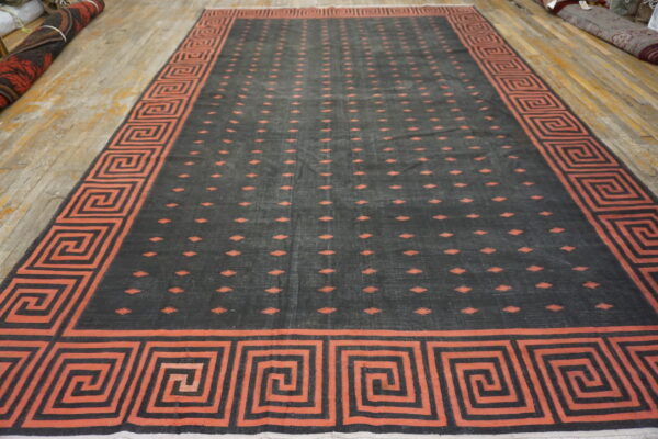 Large dark gray rug with an orange geometric border and repeating central patterns on wood flooring.