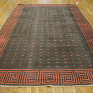 Large charcoal rug features rust Greek key border and repeating diamond pattern on a distressed wood floor.