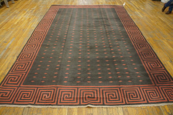 Large charcoal rug features rust greek key border and repeating diamond pattern on a distressed wood floor.