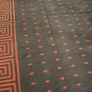 Dark rug featuring a reddish-orange Greek key border and small diamond motifs on a light-colored wooden floor.