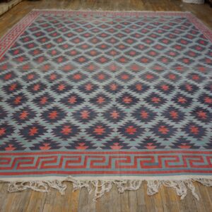 Geometric flatweave rug in blue, coral, and navy with a Greek Key border on wood plank flooring.
