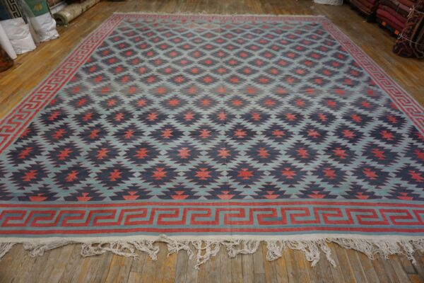 Geometric flatweave rug in blue, coral, and navy with a greek key border on wood plank flooring.