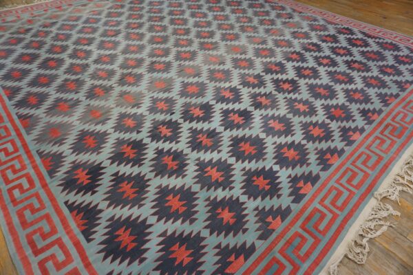A low-pile geometric rug in teal, navy, and coral features zigzag patterns and a meander border on a wood floor.