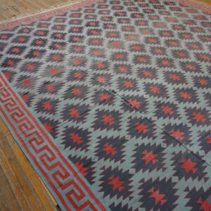 Blue, navy, and coral geometric flatweave rug with a Greek key border displayed on distressed wood planks.