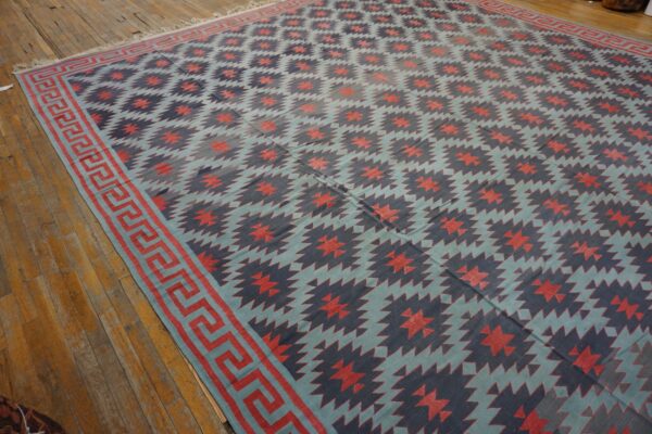 Blue, navy, and coral geometric flatweave rug with a greek key border displayed on distressed wood planks.