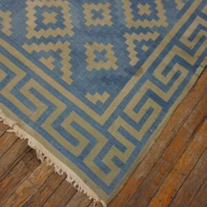Blue and khaki geometric rug featuring a Greek key border on distressed wood plank flooring.