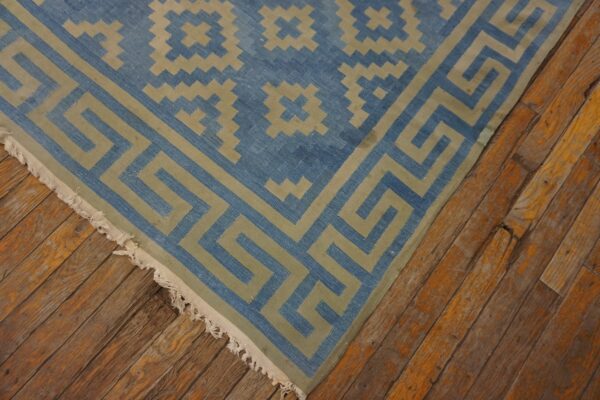 Blue and khaki geometric rug featuring a greek key border on distressed wood plank flooring.