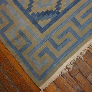 Flatweave rug with a blue and khaki geometric border rests on distressed hardwood flooring.