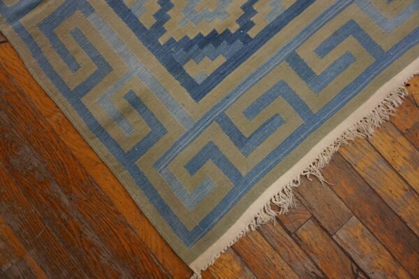Flatweave rug with a blue and khaki geometric border rests on distressed hardwood flooring.