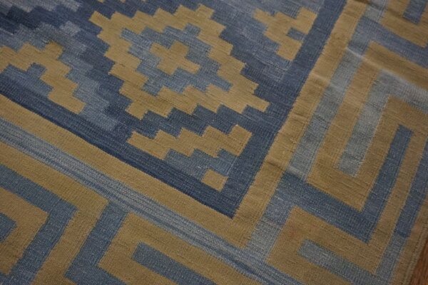 Blue and tan flatweave rug featuring a geometric pattern of stepped diamonds and angular borders.