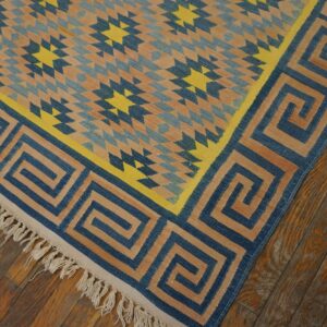 Blue, tan, and yellow flatweave rug with a geometric star pattern and Greek key border on wood flooring.