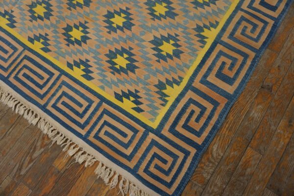 Blue, tan, and yellow flatweave rug with a geometric star pattern and greek key border on wood flooring.