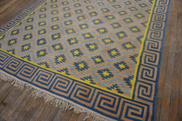Blue, tan, and yellow flatweave rug featuring a geometric pattern and a greek key border on wood flooring.