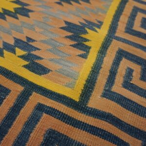 Angular geometric rug in blue, tan, and yellow features Greek key and diamond patterns.