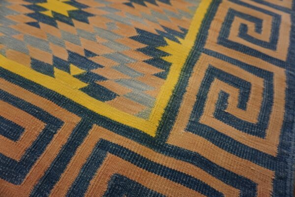 Angular geometric rug in blue, tan, and yellow features greek key and diamond patterns.