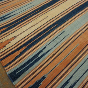 Navy, burnt orange, light blue, and cream striped flatweave rug visible on worn hardwood floors.