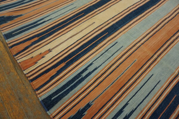 Navy, burnt orange, light blue, and cream striped flatweave rug visible on worn hardwood floors.