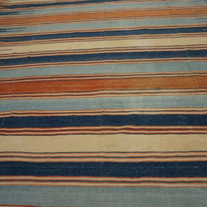 Flatweave rug with horizontal stripes in indigo, rusty orange, pale blue, and cream on wood floors.