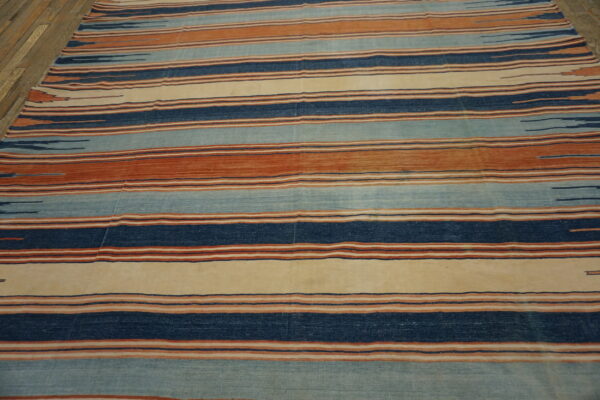 Flatweave rug with horizontal stripes in indigo, rusty orange, pale blue, and cream on wood floors.