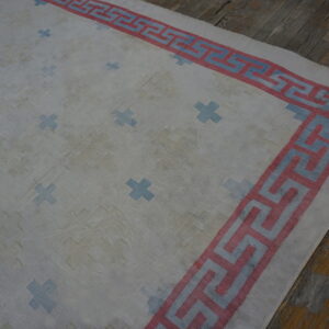 White rug featuring blue plus signs and a pink and blue Greek Key border, lying on distressed wood flooring.