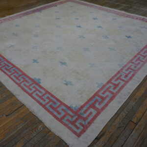 Pale rug with blue crosses and a bold red and blue geometric border on distressed wood flooring.