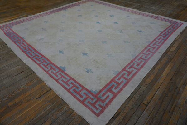 Pale rug with blue crosses and a bold red and blue geometric border on distressed wood flooring.