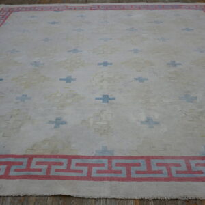Flatweave white rug with blue crosses and a red meander border displayed on dark wood flooring.