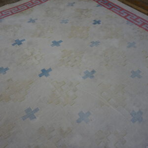 Light rug with blue cross motifs, yellow repeating geometrics, and a red Greek key border on wood flooring.
