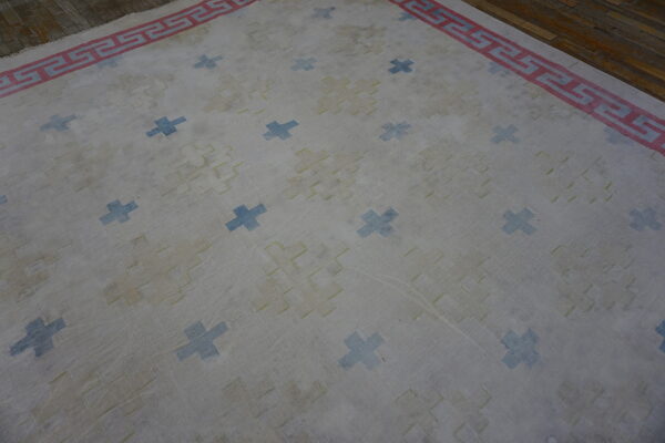 Light rug with blue cross motifs, yellow repeating geometrics, and a red greek key border on wood flooring.