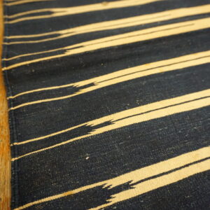 Close-up of a navy and cream flatwoven rug with jagged stripes next to worn wood floorboards.