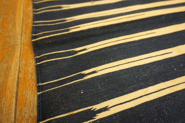 Close-up of a navy and cream flatwoven rug with jagged stripes next to worn wood floorboards.