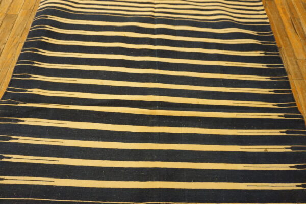 Flatwoven rug with thick, irregular dark blue and cream horizontal stripes on wood planks.