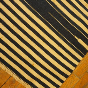 Flatweave rug featuring black and yellow-beige diagonal stripes with fringe, resting on wood flooring.