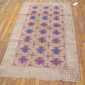 Beige rug featuring alternating blue and purple floral medallions and a Greek key border on wood floor.